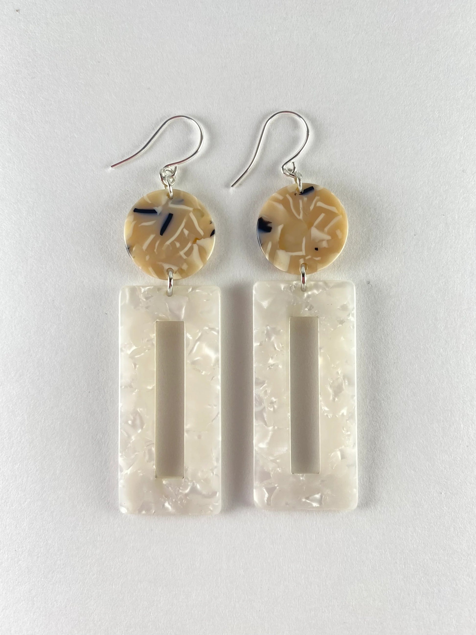 Dangling earring with 2 geometric beads.  One a dime sized marble midnight blue, beige and white bead with a large pearl white rectangle shaped donut bead. 