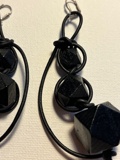 Close-up of Black geometric earrings on a textured off-white background.