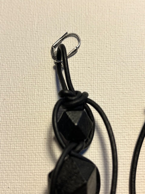 Black geometric earrings on a textured off-white background.