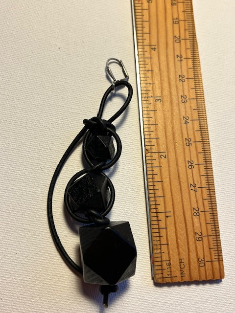 Black geometric earrings on a textured off-white background next to a wooden ruler.